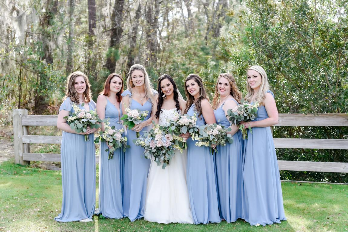 Bridal party dressed in dusty blue dresses pose with brunette bride