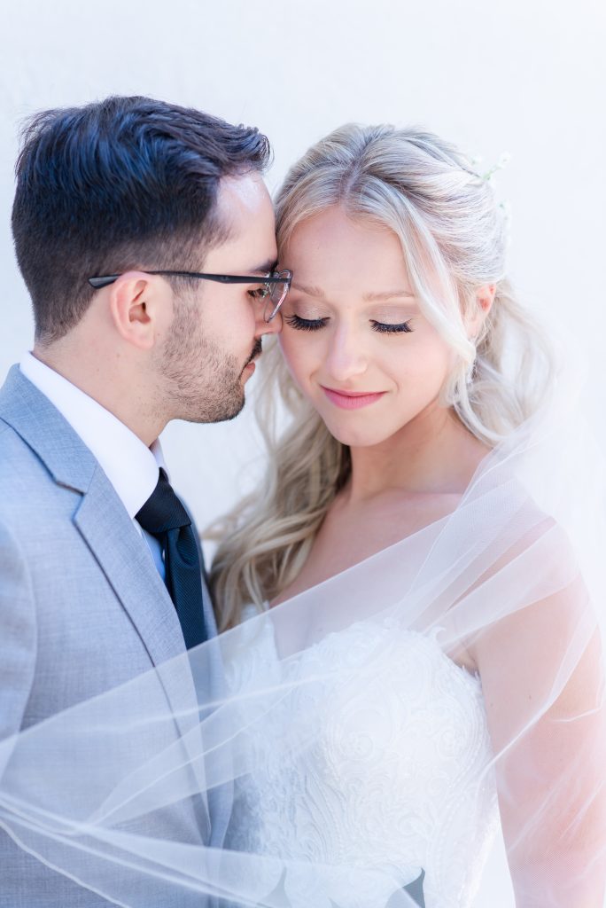 groom nuzzles bride while veil swoops over both of their shoulders