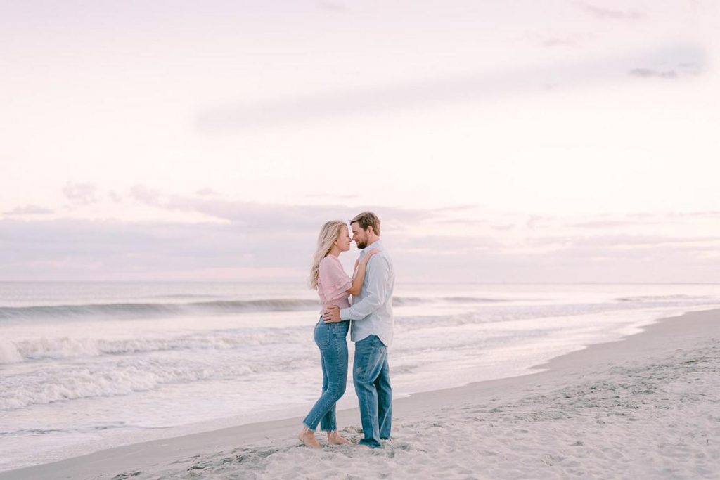 engaged couple embrace nose to nose during pink sunset at beach