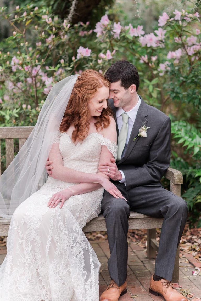 Newlywed couple snuggle on park bench surrounded by pink flowers