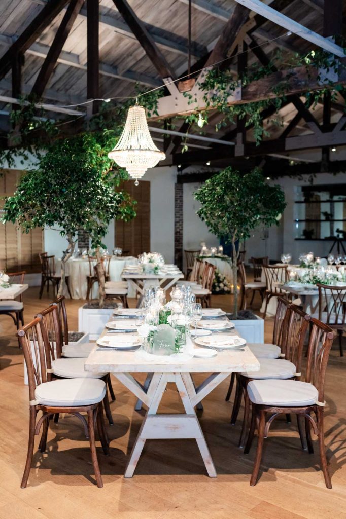 Interior photo of the inside of Cannon Green wedding venue reception space with greenery, chandeliers, tables