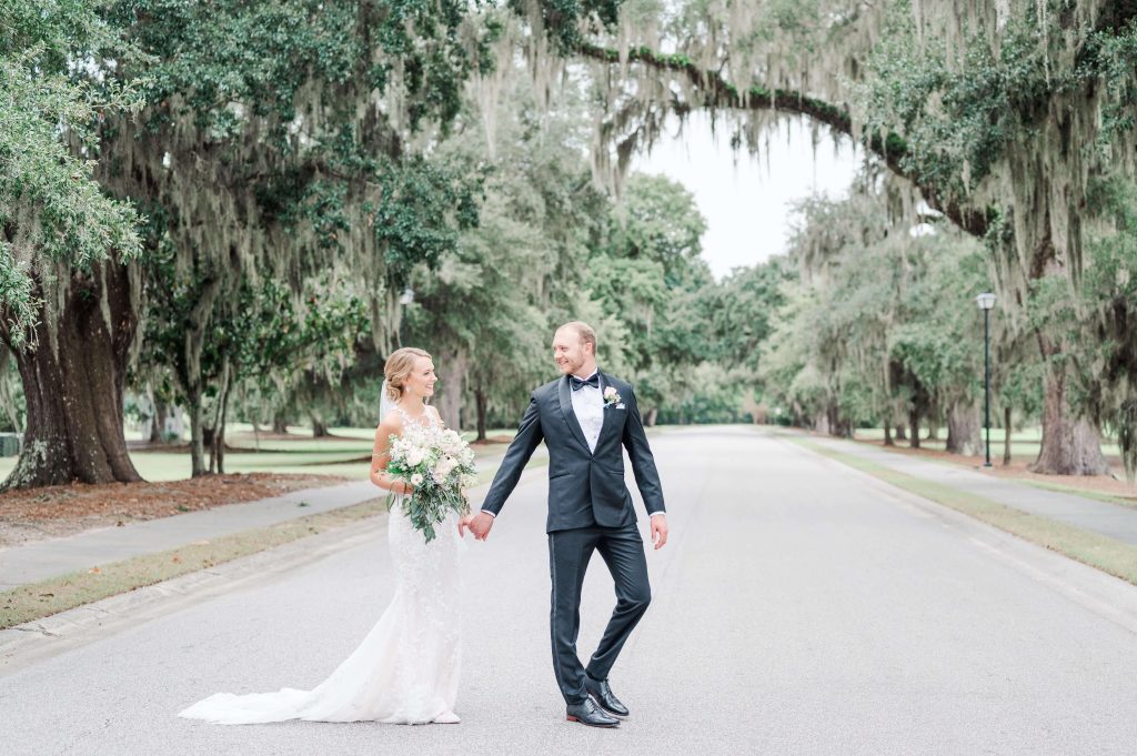 Groom leads bride across street under oak trees