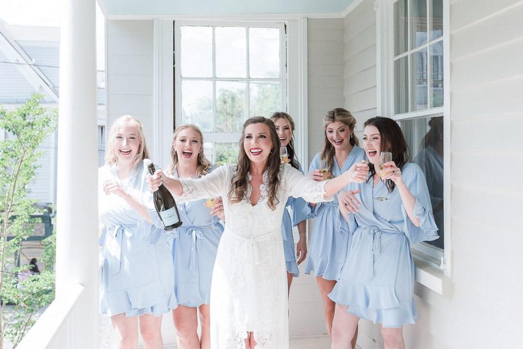 bride popping champagne on porch with bridesmaids while in robes