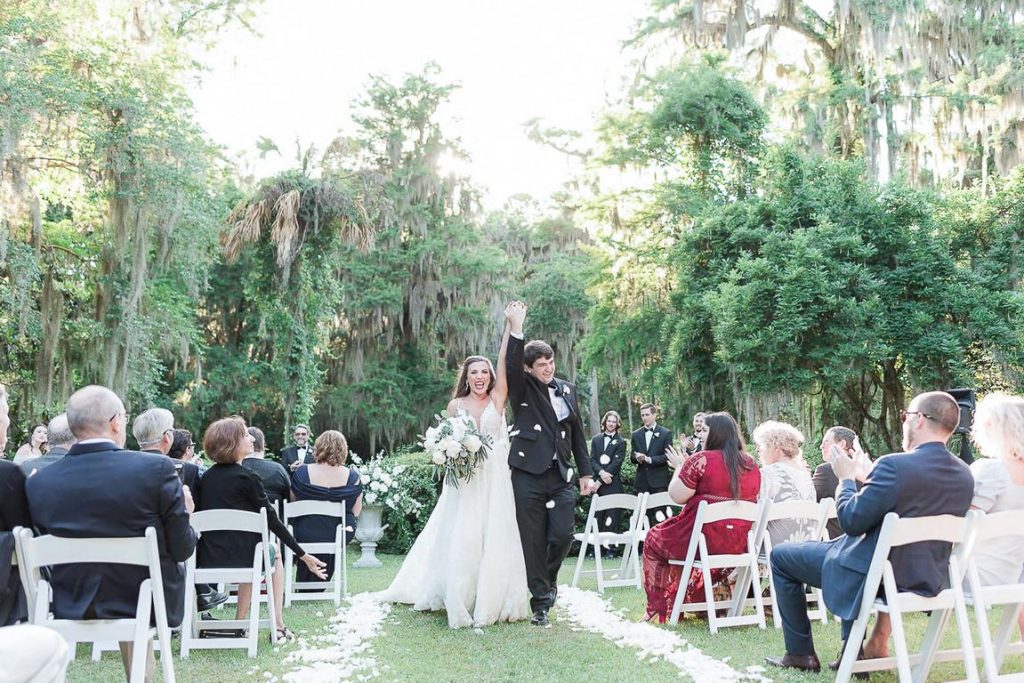 Newlyweds recessing down aisle hold hands up in the air at Charleston Wedding