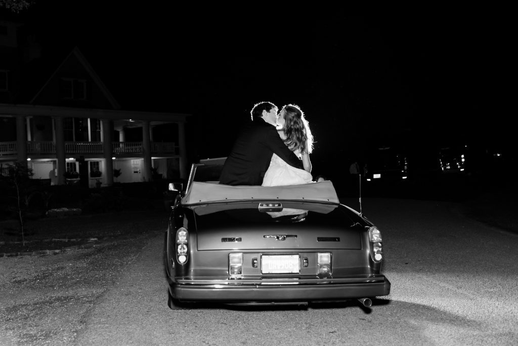 newlyweds sitting on top of back of convertible share a kiss