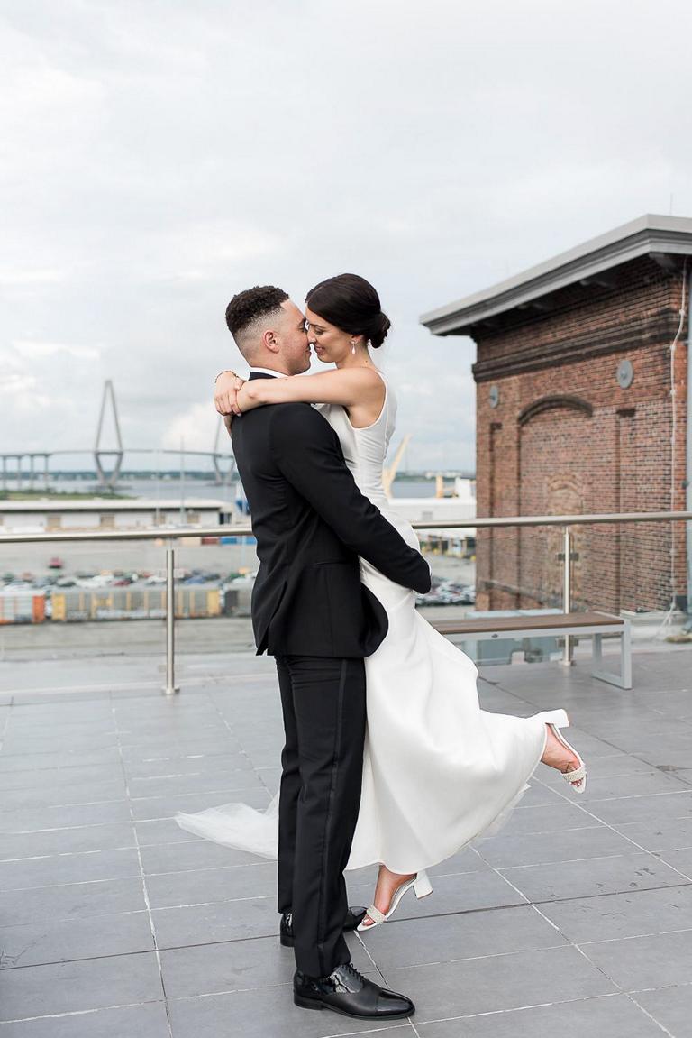 groom lifts bride up for a kiss on rooftop of Cedar Room