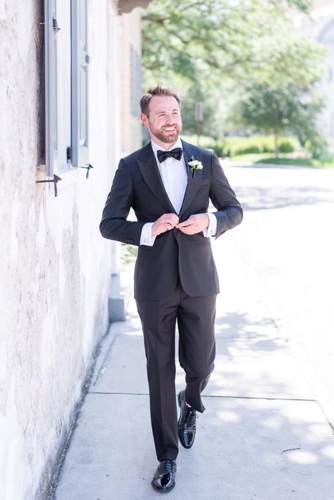 Groom looking off camera walking and buttoning black tuxedo jacket