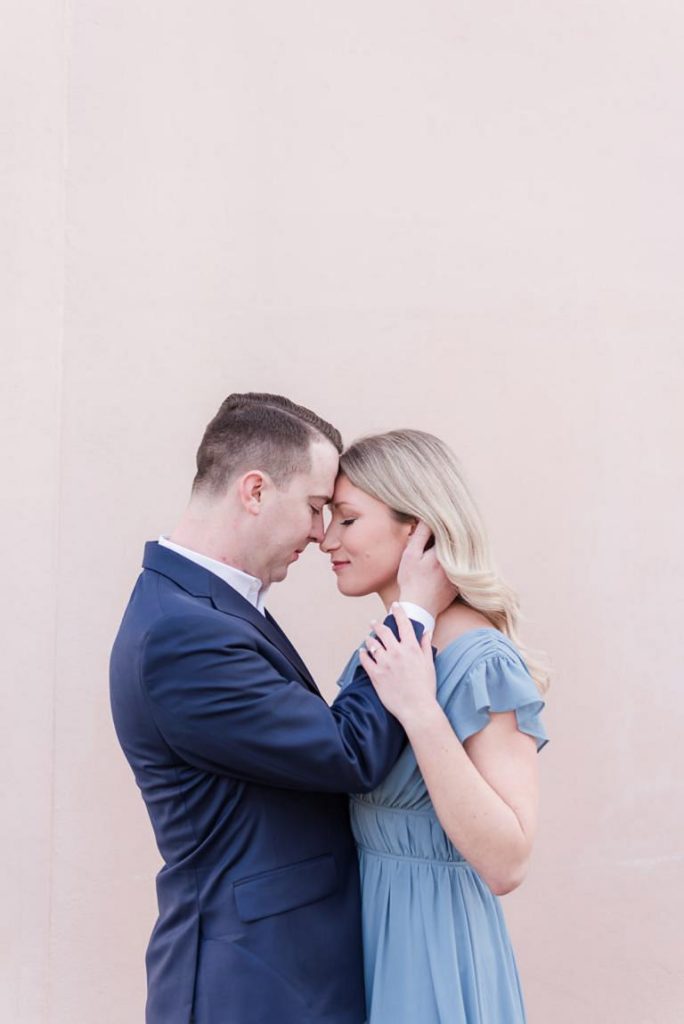 guy with hand in girl's hair pulling her close stand in front of pink building