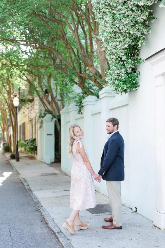 engaged couple walking away hand in hand looking back at camera