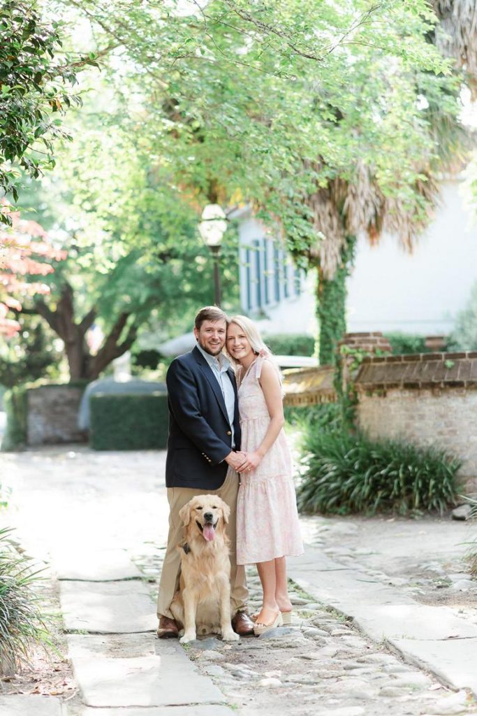 Engaged Couple and their dog stand in Charleston cobblestone alley