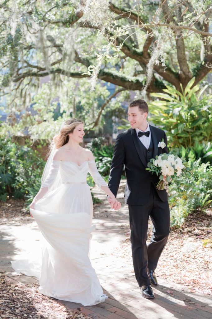 bride and groom walking through St. Luke's Chapel Garden holding hands
