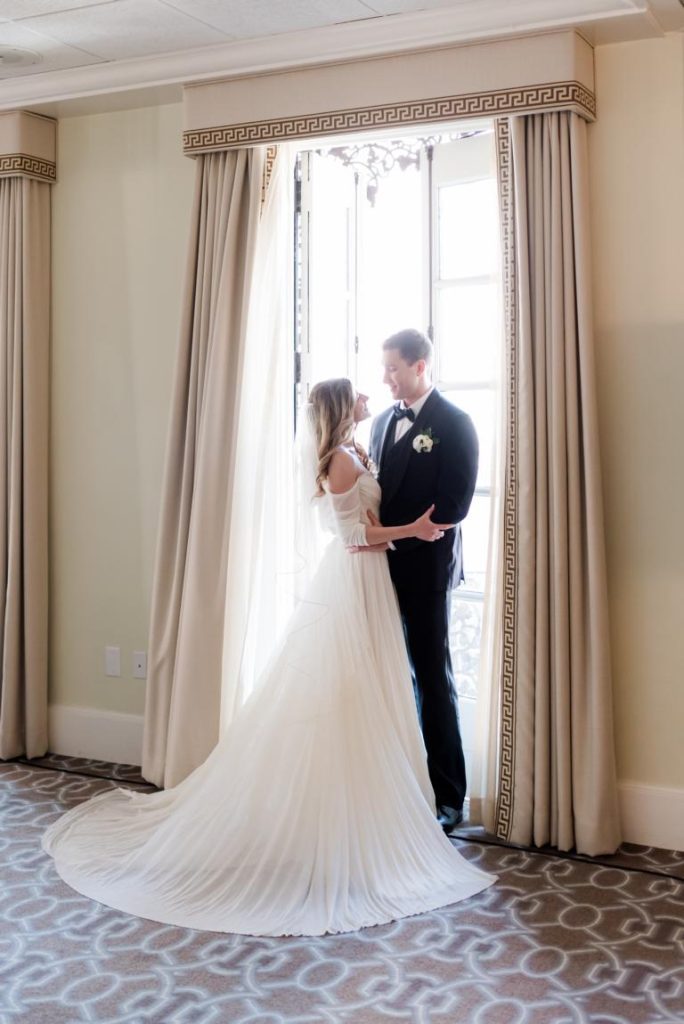 newlyweds holding each other in front of large window