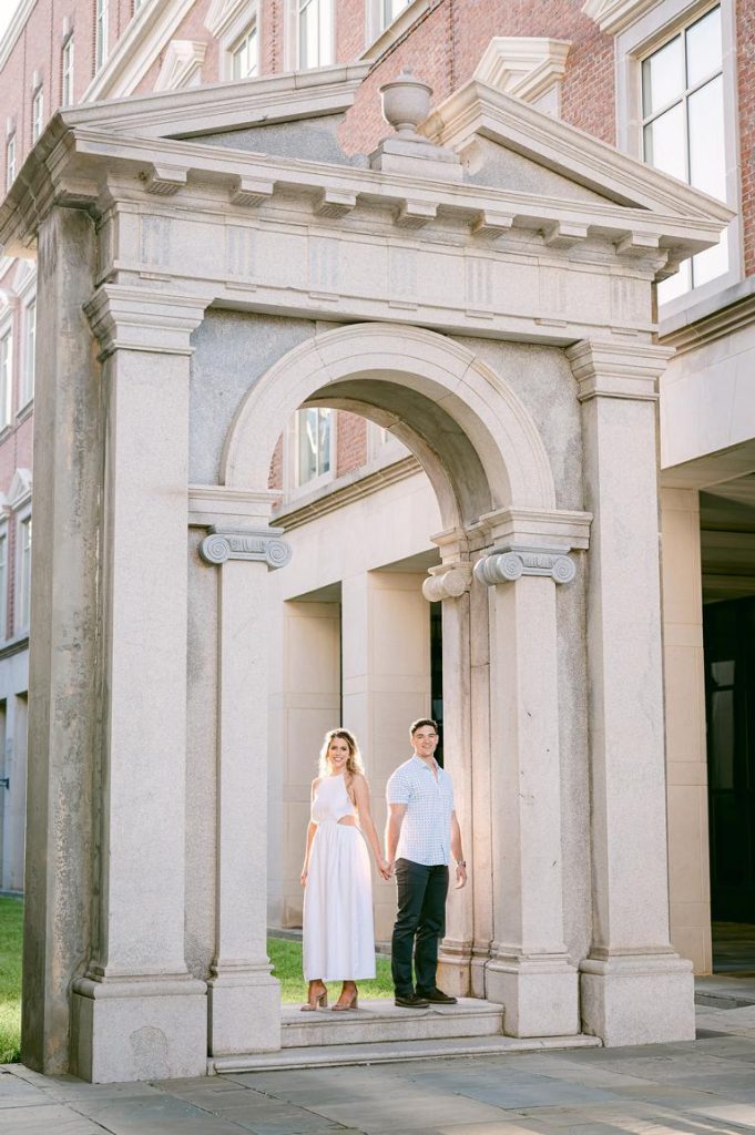 couple stand hand in hand under arch