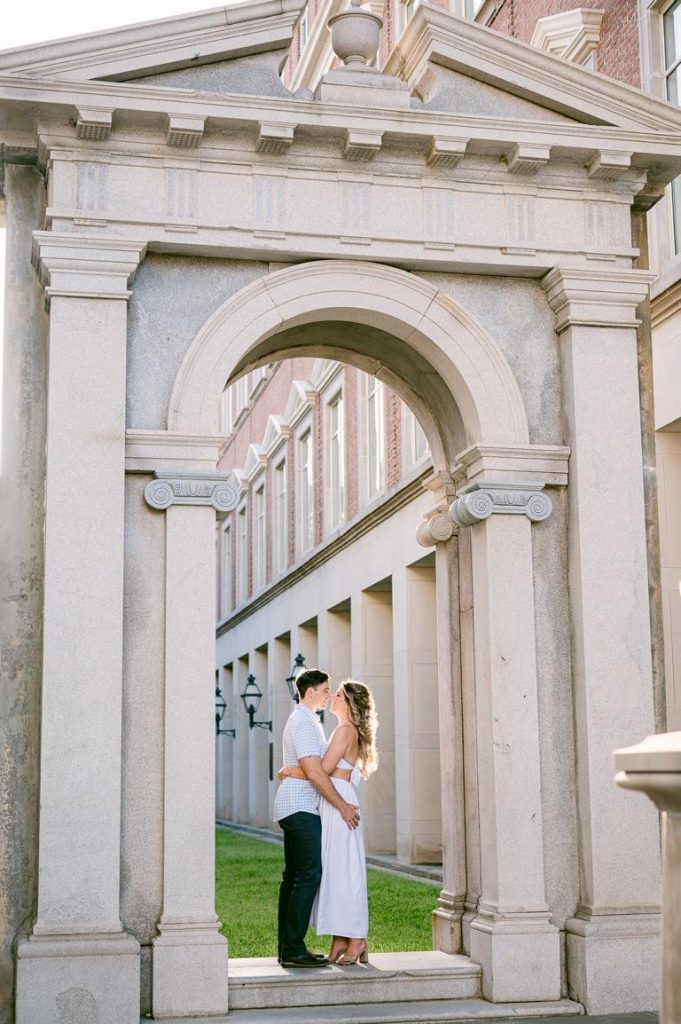 couple hold each other around the waists while standing under arch