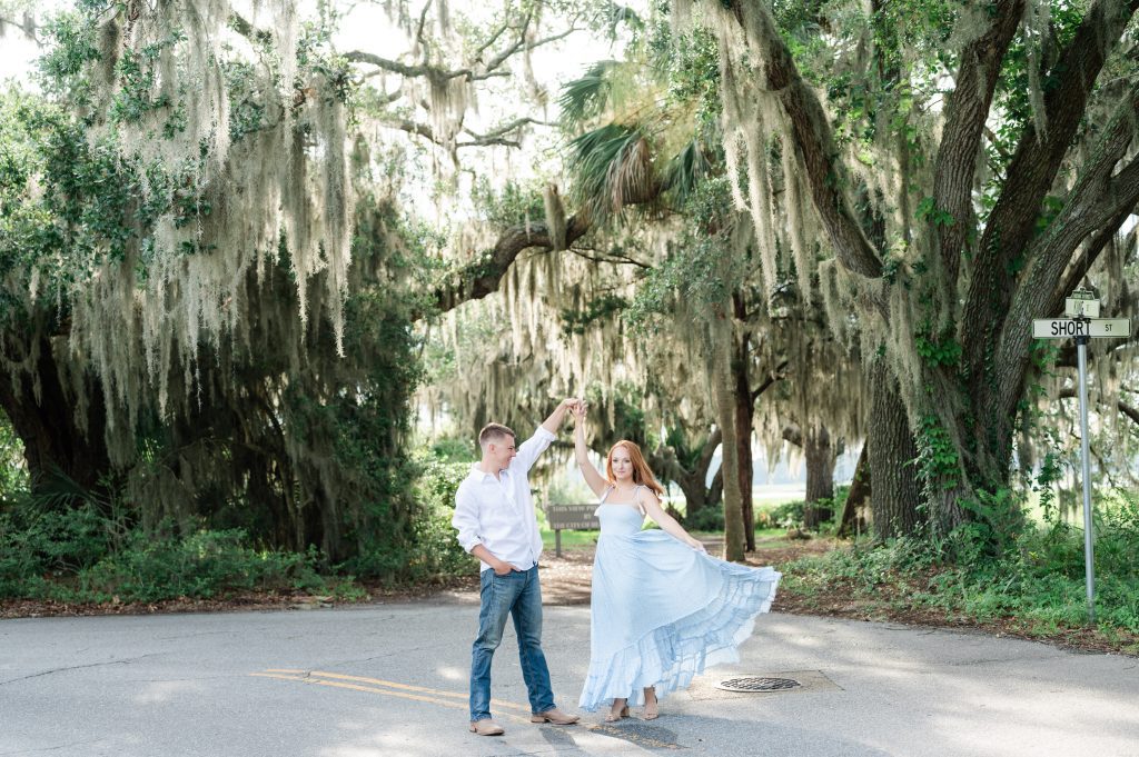 guy twirling girlfriend in street in front of oak trees