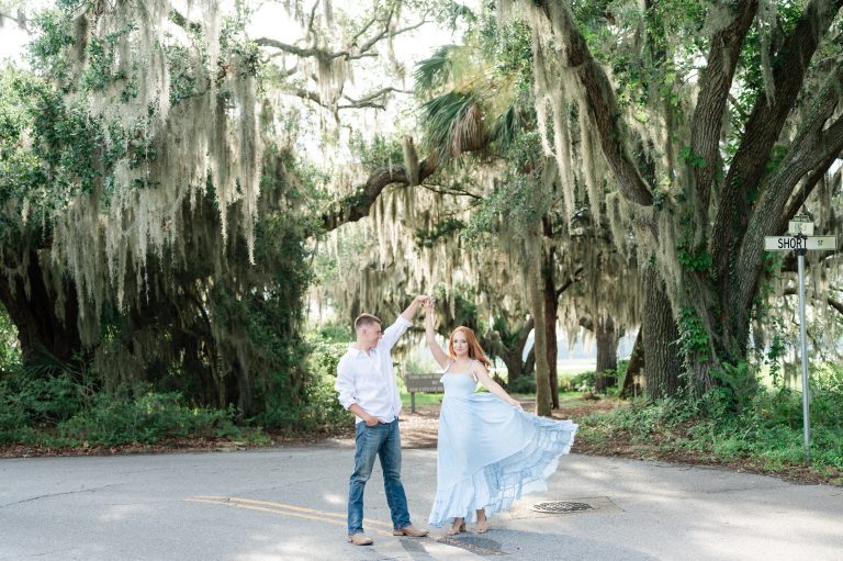 guy twirling girlfriend in street in front of oak trees