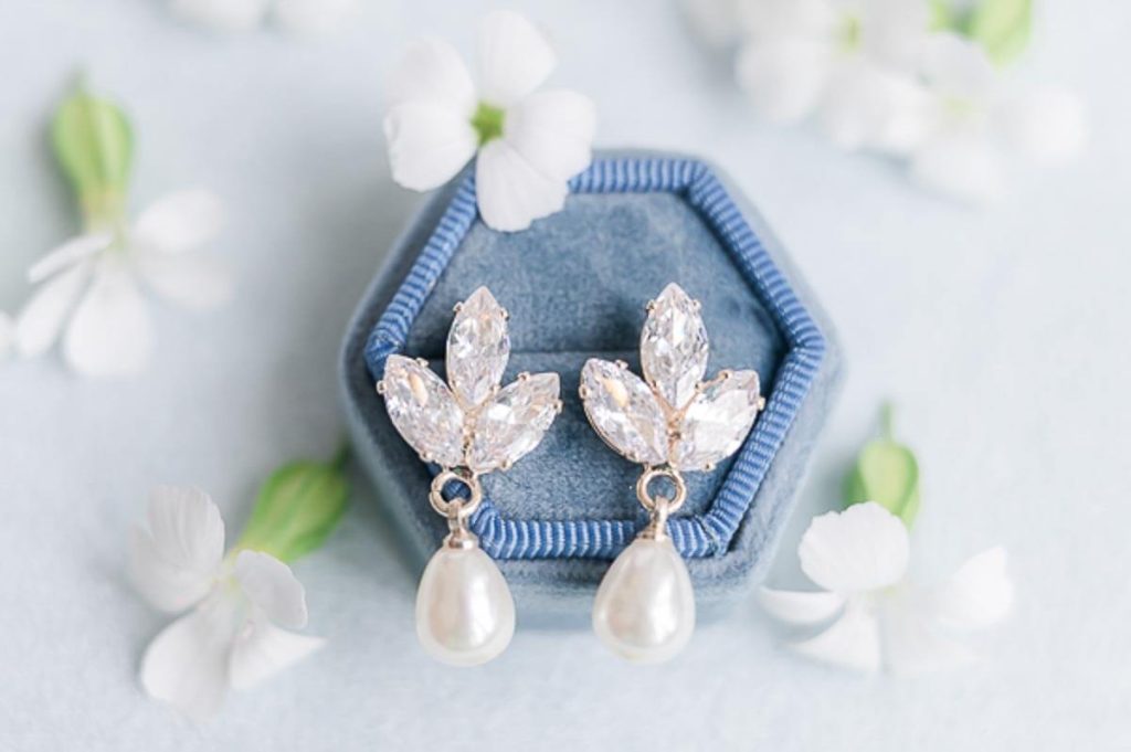 pearl and crystal earrings in blue ring box with flower petals surrounding them