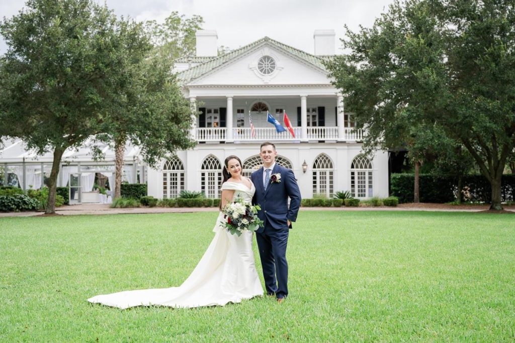 bride and groom stand together on lawn in front of Lowndes Grove Plantation House