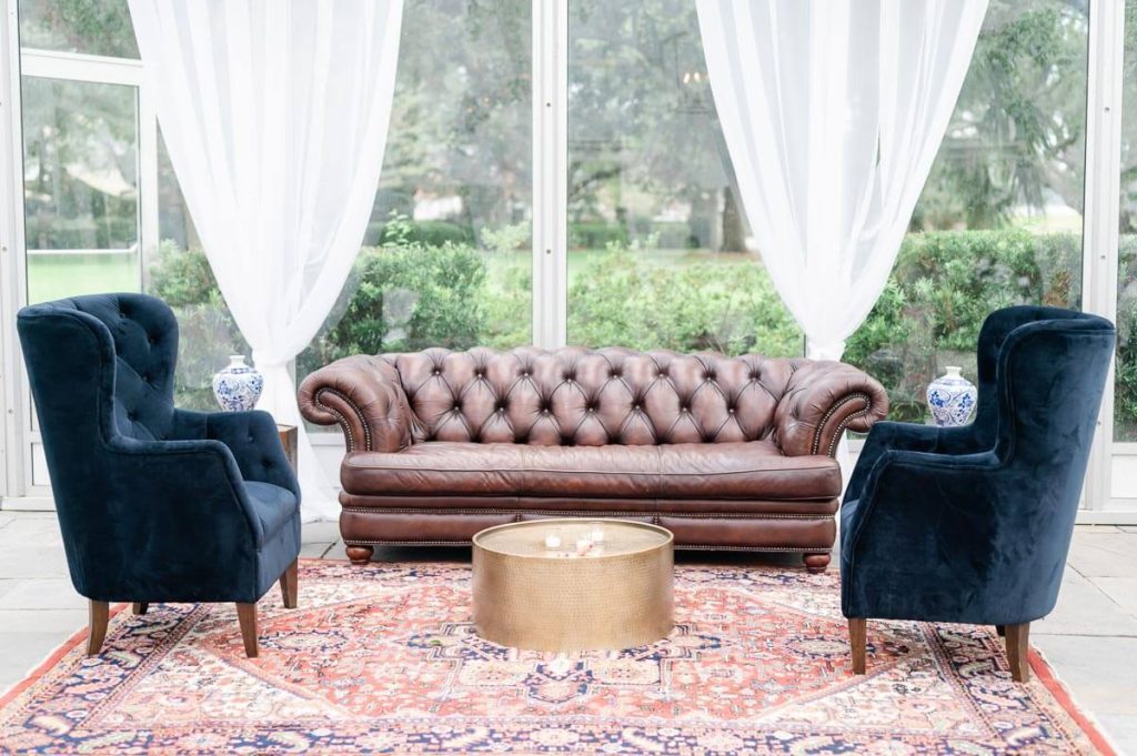 Tufted brown leather couch and two blue velvet chairs set up at wedding reception
