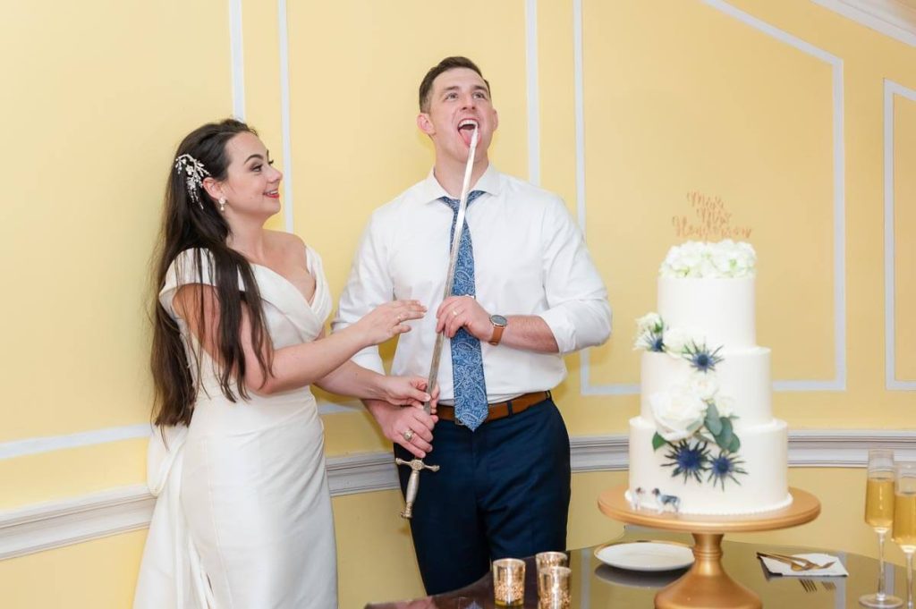 groom licks wedding cake off of sword
