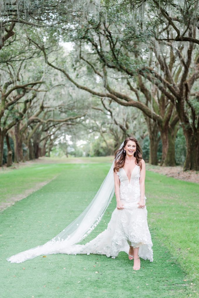 bride holding wedding dress running in avenue of oaks