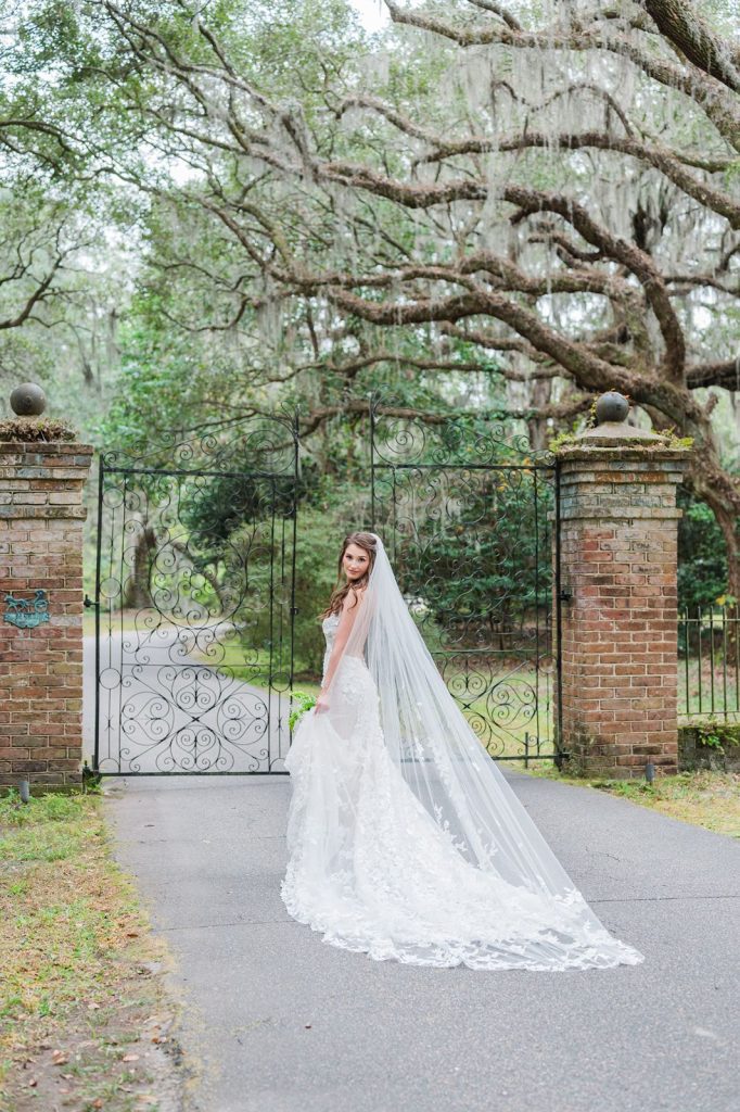bride walking towards iron gate at Legare Waring House holding dress