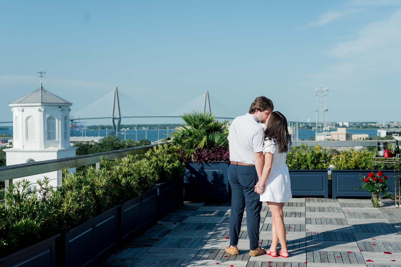 couple kiss on a rooftop with the Ravenel Bridge in the background