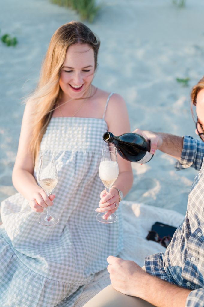 guy pours champagne for new fiancé at beach