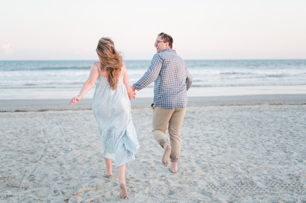newly engaged couple run hand in hand towards the ocean at Isle of Palms beach