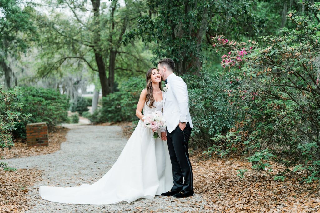 groom whispers in bride's ear on gravel path in garden