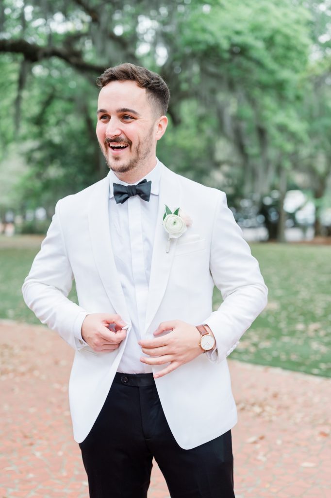 groom looking off camera while buttoning white tuxedo jacket