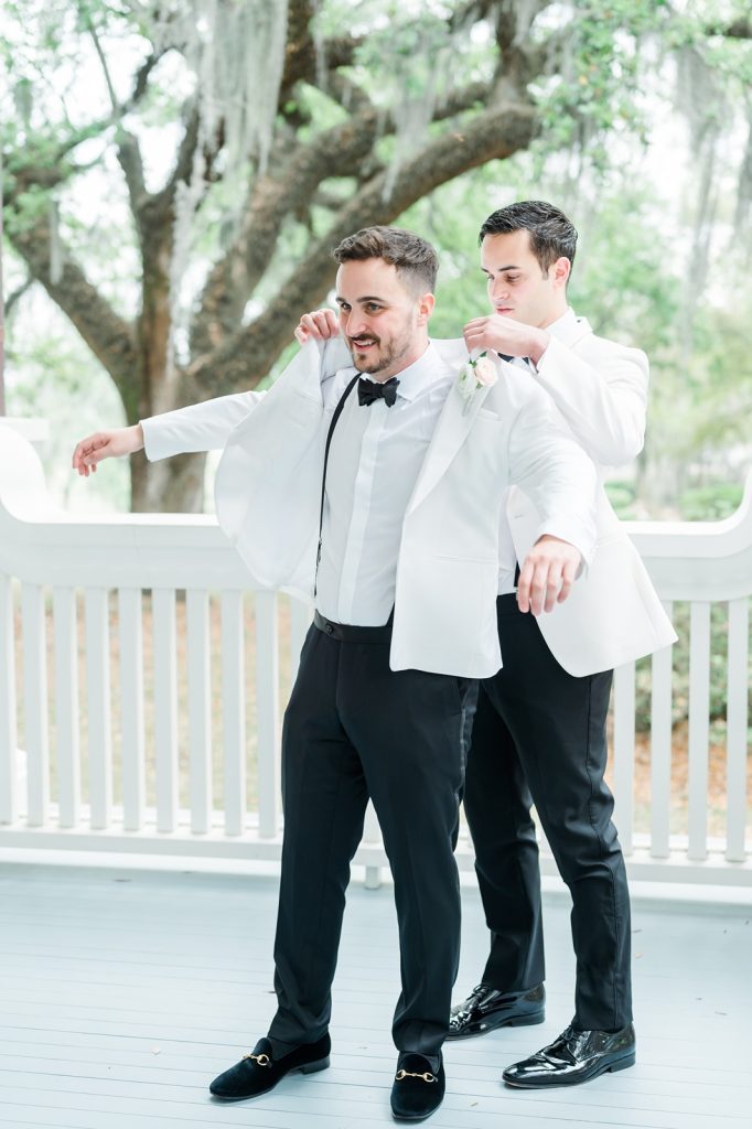 brother helping groom put on white tuxedo jacket