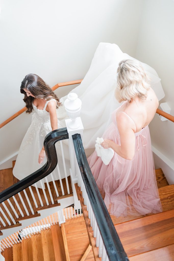 sister holding bride's dress up as she walks down the stairs