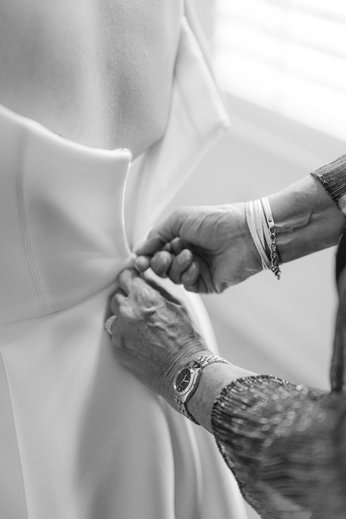close up of mother's hand zipping up daughter's wedding dress