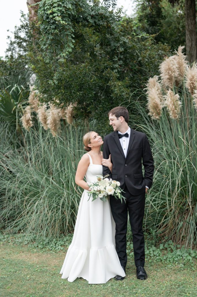 bride and groom look at each other in front of pampas grass