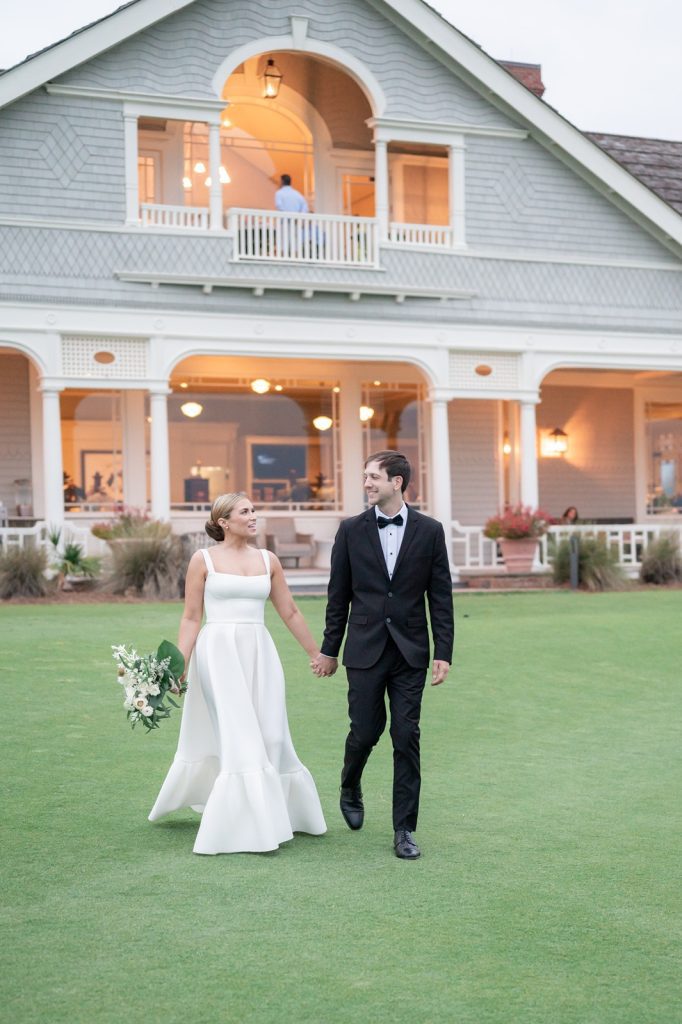 newlyweds walk hand in hand away from the back of the clubhouse
