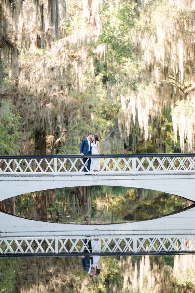 far away photo of couple kissing on white bridge and their reflection showing in the water below