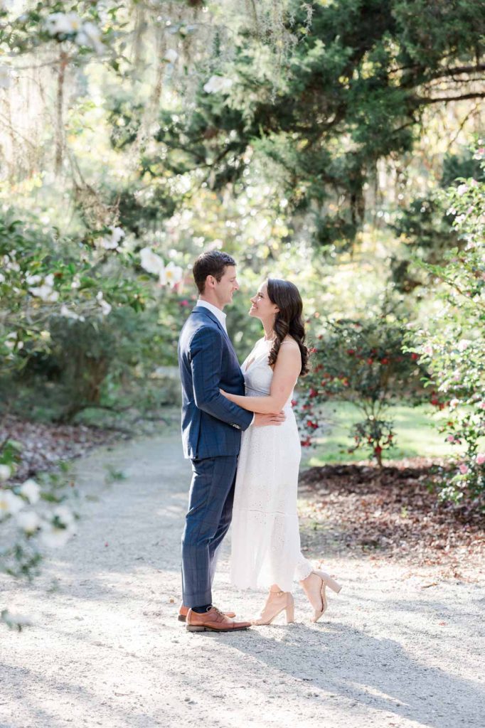 couple embrace and look into each other's eyes while standing on a gravel path in garden