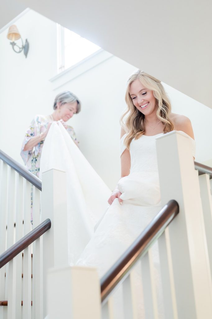 mother holds daughter's wedding dress as she walks down the stairs