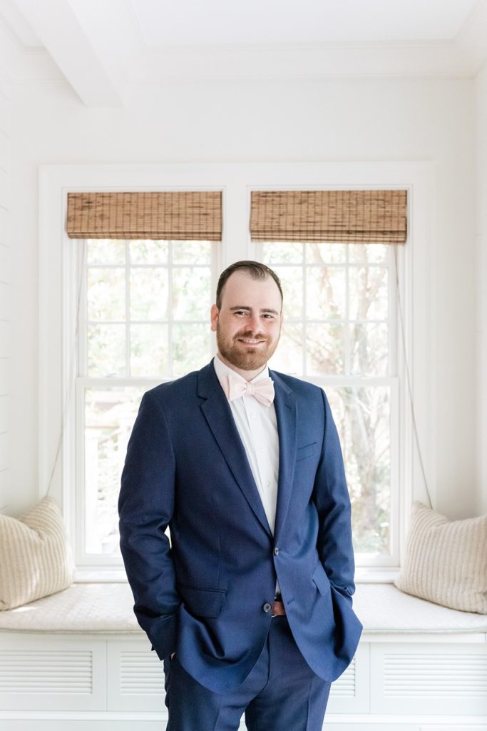 groom in blue tux standing with hand in pockets inside house