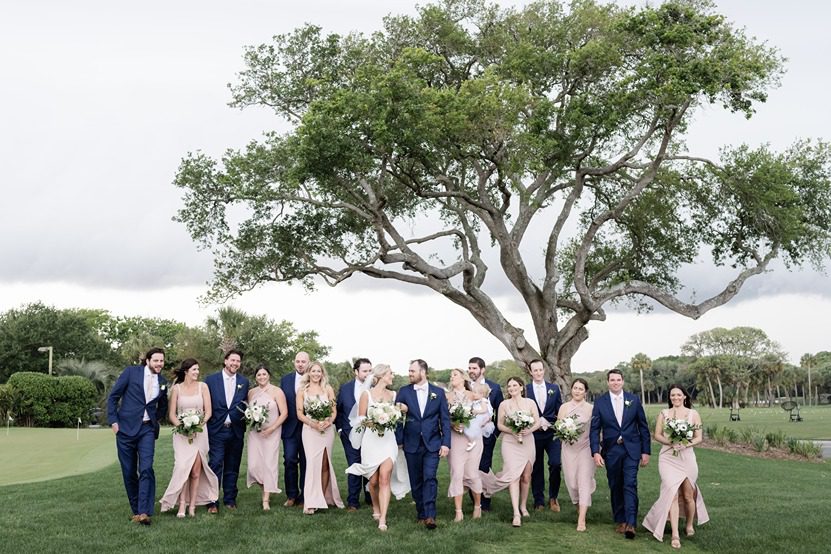large wedding party walk arm in arm under oak tree