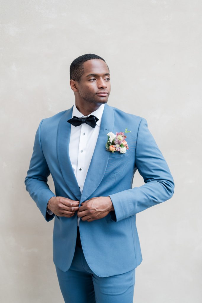 groom buttoning blue shawl tuxedo coat looking off camera