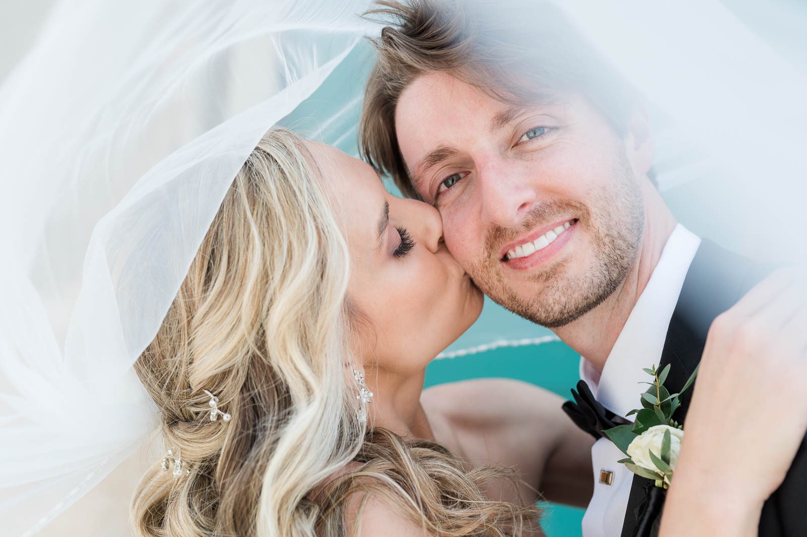 bride kisses groom on cheek under her veil