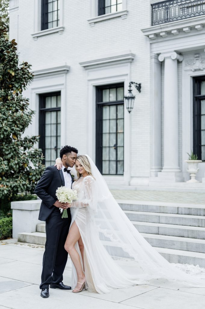 bride and groom pose in front of a mansion