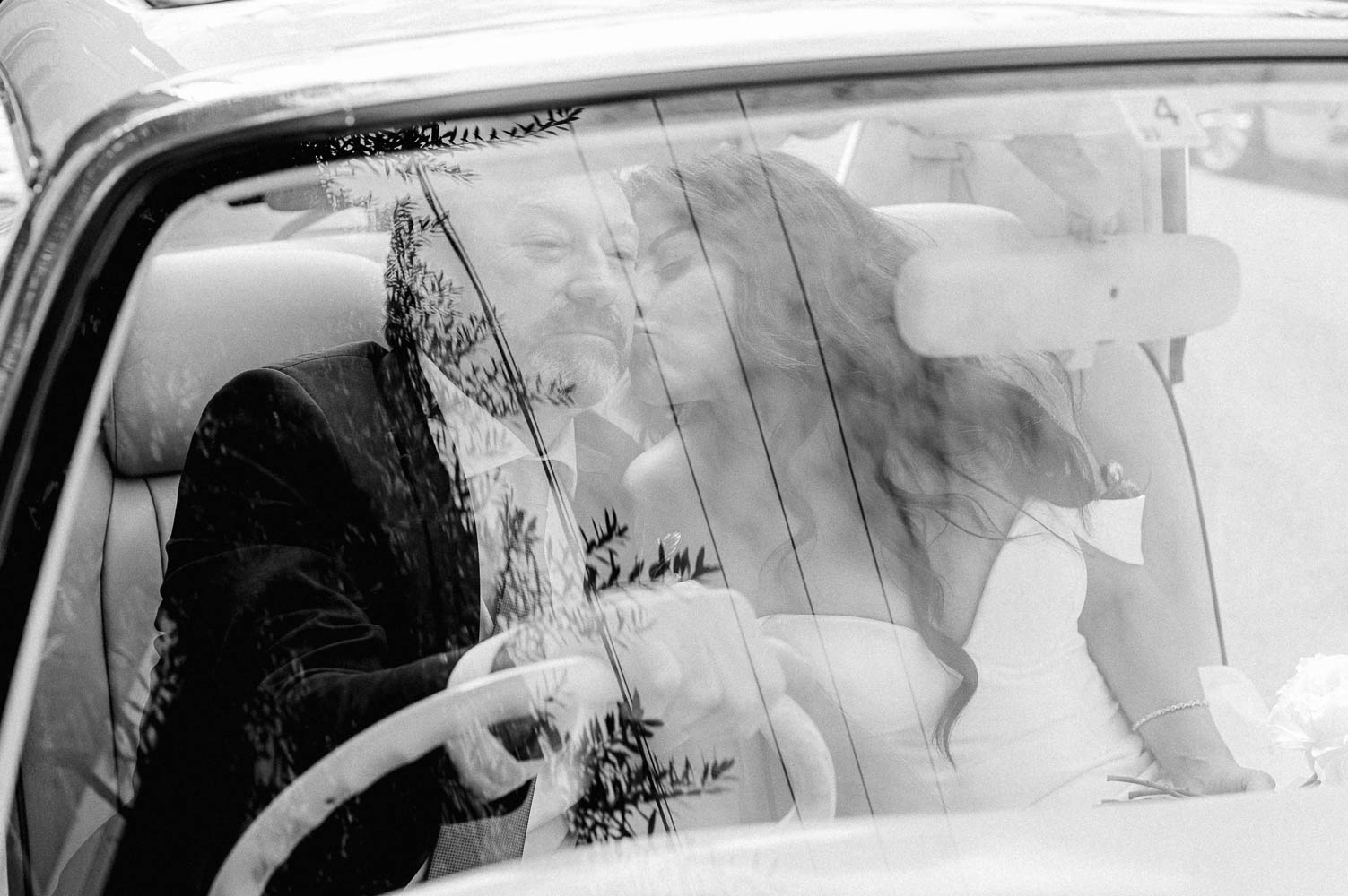 bride kisses groom on cheek, see through windshield of The Pink Figgy Car