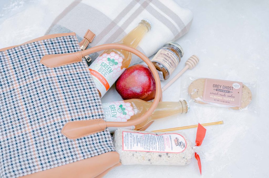 houndstooth bag filled with picnic items with local drinks, cookies, and apple