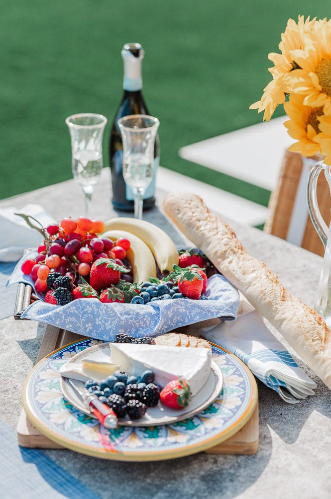 picnic spread of fruit, cheese, baguette, and champagne