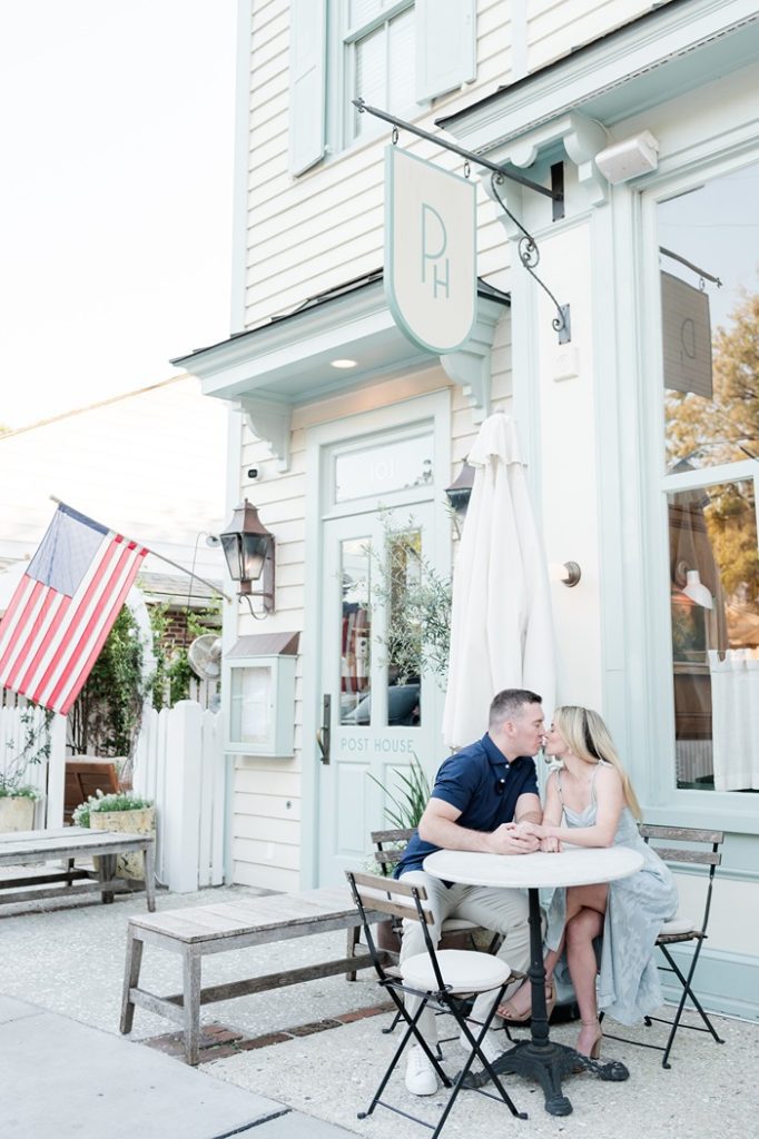 engaged couple kiss while sitting at a table outside the Post House Inn