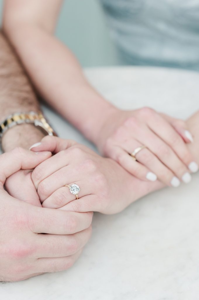 Engaged couple hold hands on top of white marble table