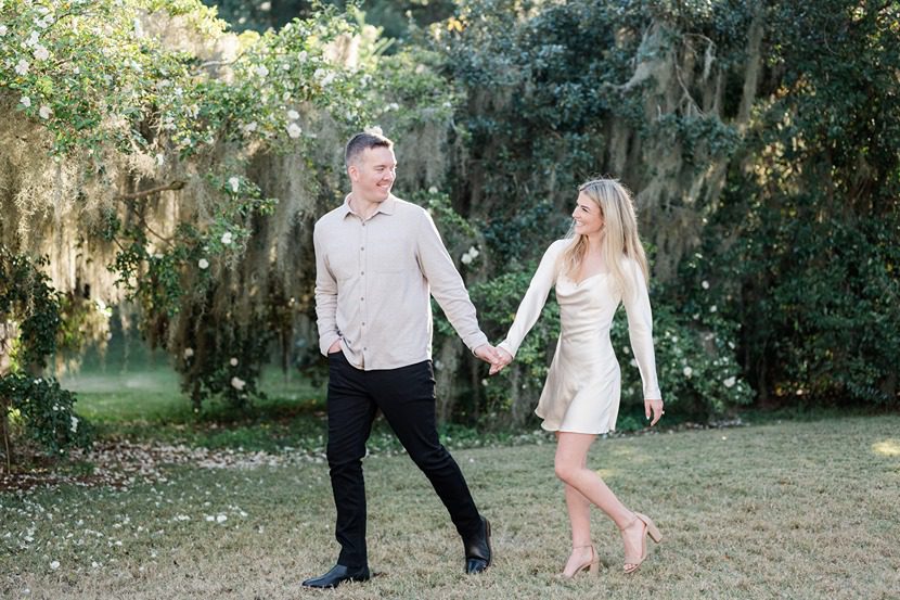 engaged couple holding hands with man leading woman around the grounds of Legare Waring